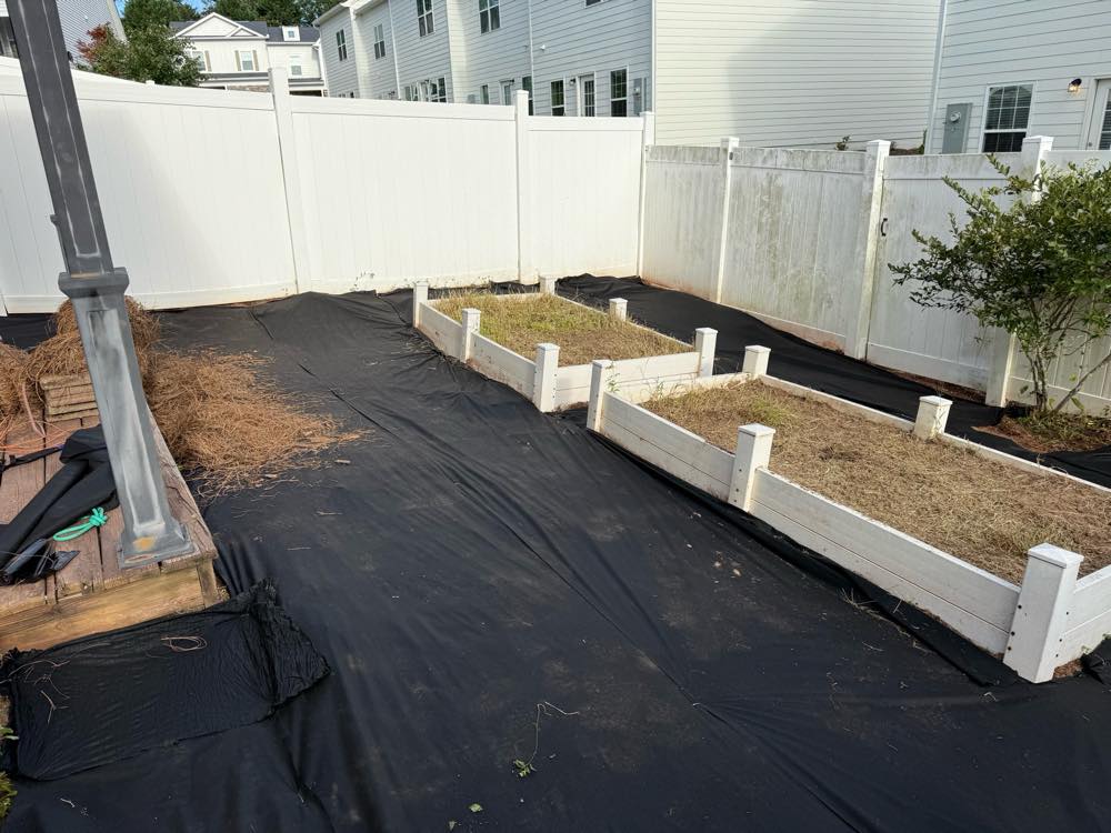 Raised garden beds and landscape fabric laid in a fenced backyard