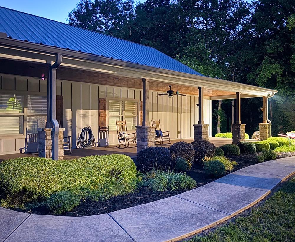 Trimmed shrubs and fresh mulch beds along a porch at dusk