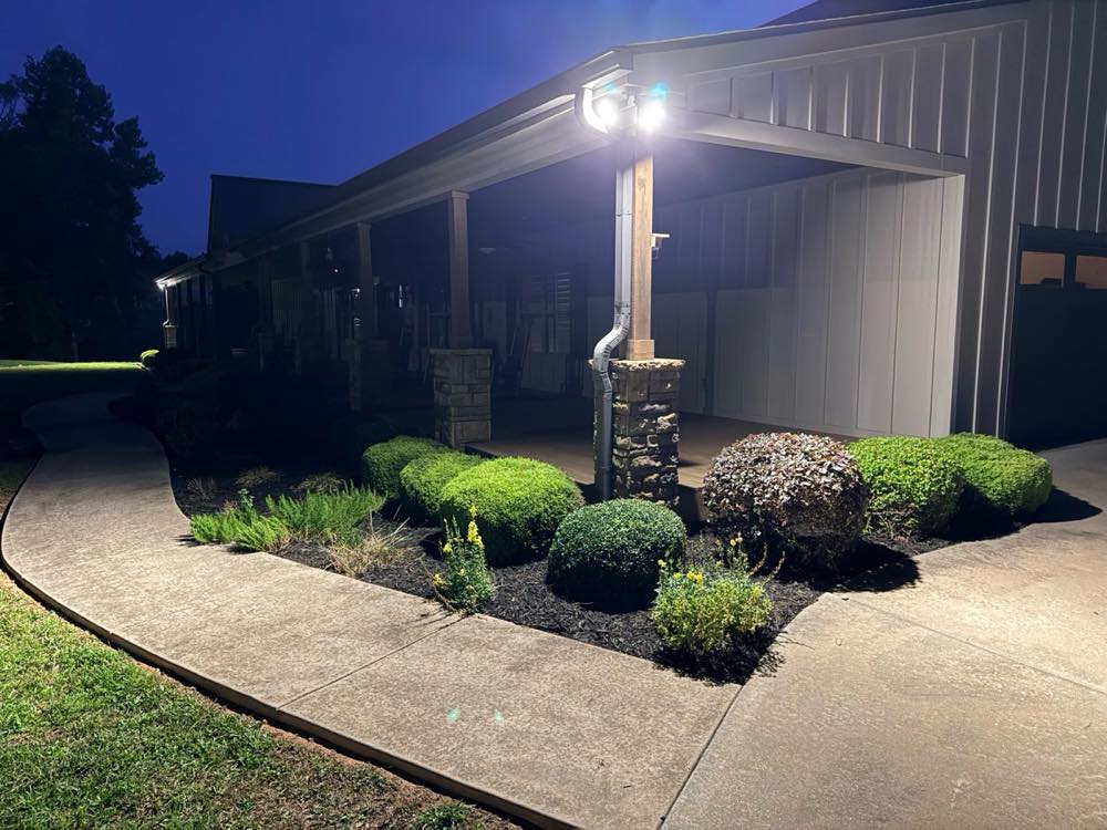 Shrubs and mulch beds along a covered porch, lit up at night